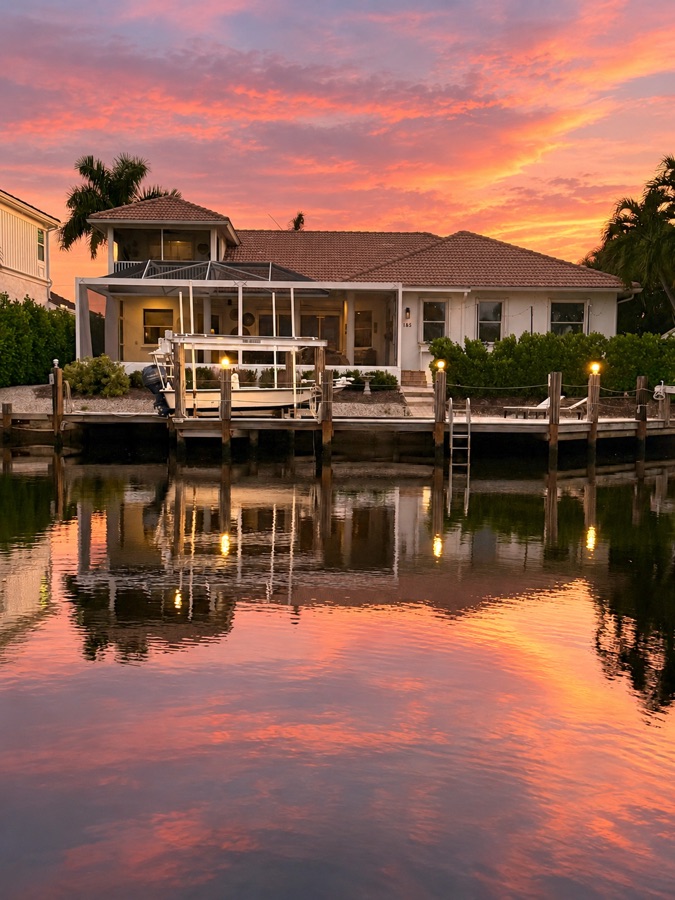 The back of the home from across the canal at sunset, with the dock and boat lift